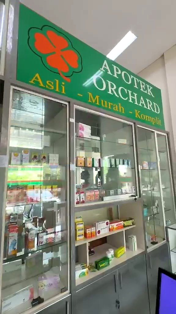Bagian dalam Apotek Orchard: papan nama hijau bermotif semanggi oranye di atas lemari kaca berisi obat